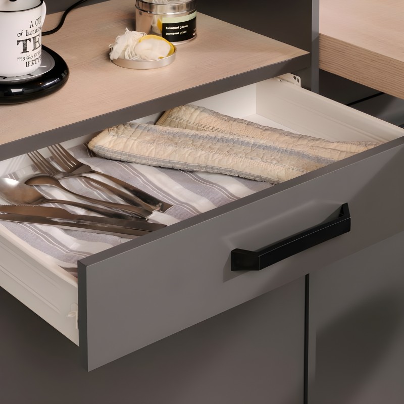 Detalle de cajón abierto en mueble de cocina blanco y gris con cubertería y textiles organizados en su interior
