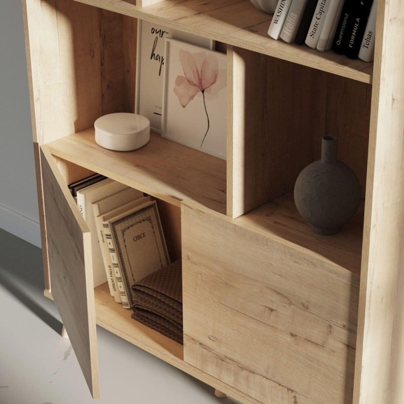 Estantería de madera clara con múltiples compartimentos abiertos y puerta inferior decorada con libros y objetos de decoración
