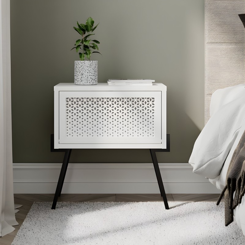 Mesita de noche blanca con frente perforado y patas negras en dormitorio junto a cama