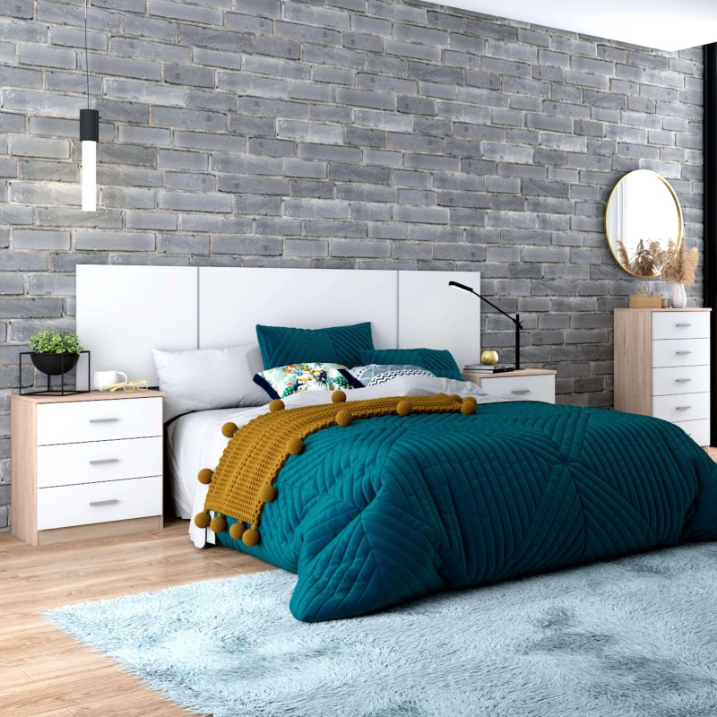 Cama con cabecero acolchado blanco y ropa de cama azul petróleo en dormitorio con mesitas y pared de ladrillo gris