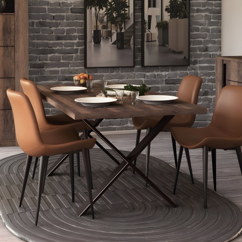 Comedor con mesa de madera oscura y patas cruzadas negras acompañada de cuatro sillas tapizadas en cuero marrón claro y patas ne