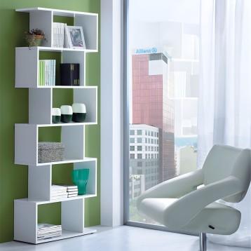 Estantería modular blanca con compartimentos asimétricos y libros y decoración en ambiente junto a sillón gris
