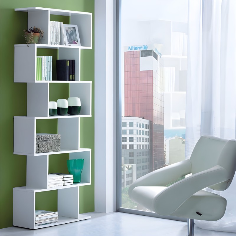 Estantería modular blanca con compartimentos asimétricos y libros y decoración en ambiente junto a sillón gris