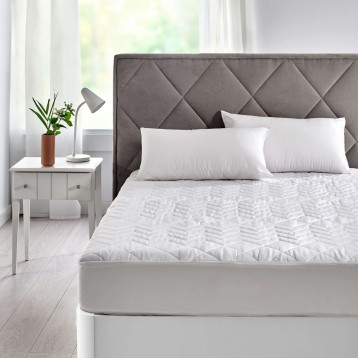 Cama con cabecero acolchado gris y protector de colchón blanco en dormitorio luminoso