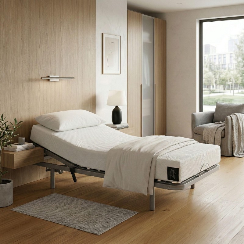Cama articulada individual con colchón blanco y estructura gris en dormitorio moderno con armario de madera clara y sillón gris