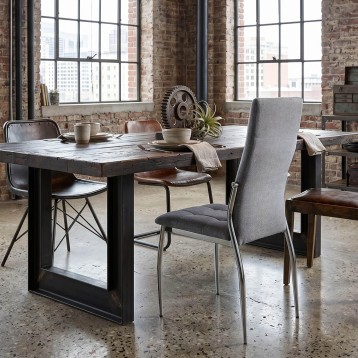 Silla tapizada en gris y tela con patas metálicas en ambiente de comedor industrial junto a mesa de madera y hierro