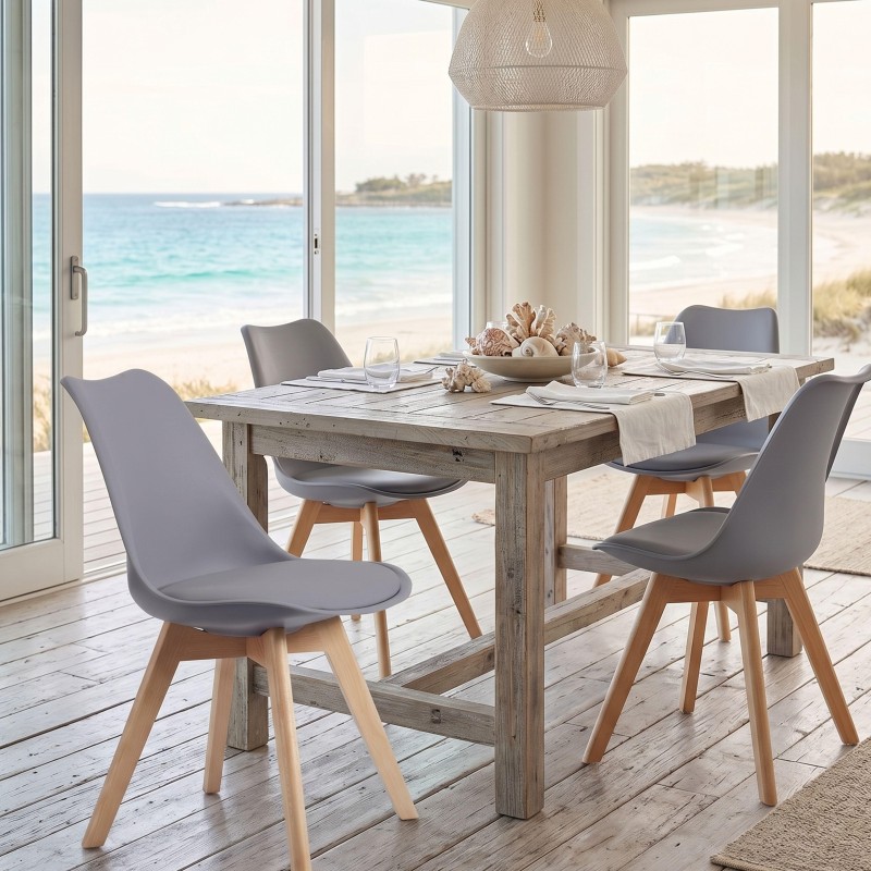 Comedor junto a ventanal de playa con mesa de madera clara y cuatro sillas gris oscuro con patas de madera natural