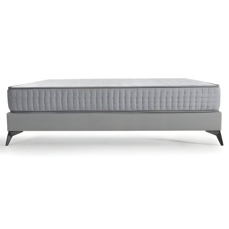 Cama con somier tapizado gris y colchón acolchado blanco patas de madera negra vista lateral