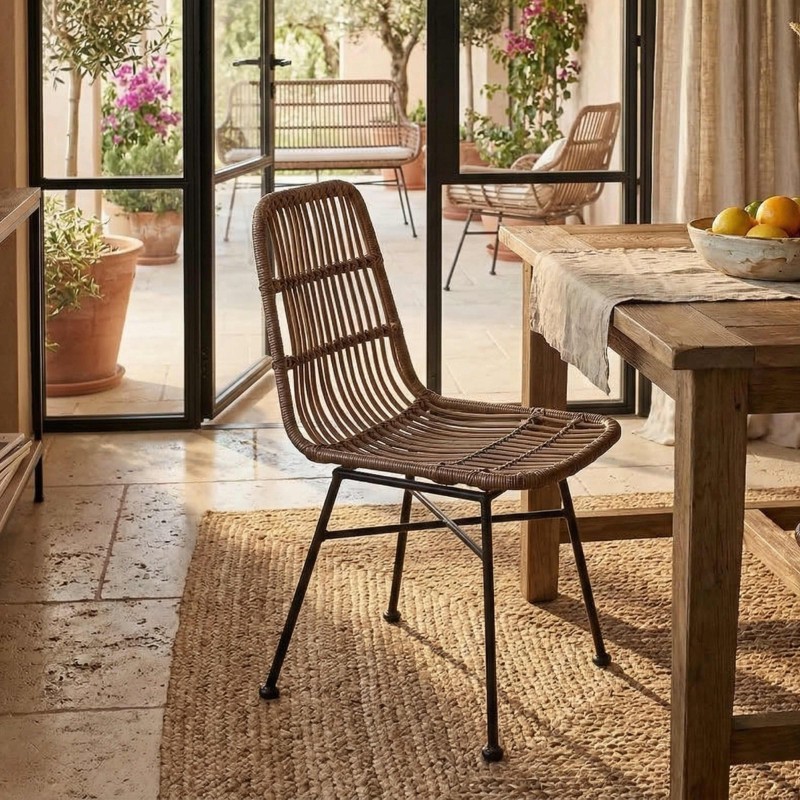 Silla de ratán marrón con patas metálicas negras en ambiente de comedor junto a mesa de madera y vistas a terraza