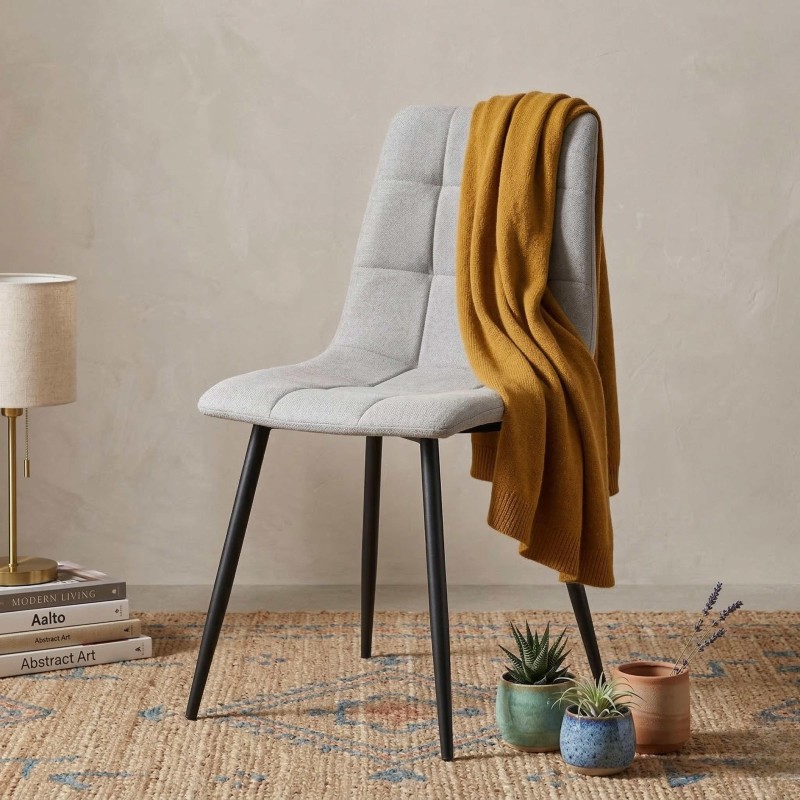 Silla de comedor tapizada en gris claro con respaldo acolchado y patas negras en ambiente decorado con manta mostaza y accesorio