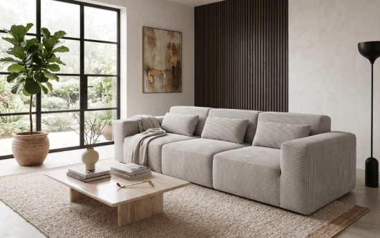 Sofá modular de pana gris claro en salón moderno con panel de madera oscura, planta y mesa de travertino