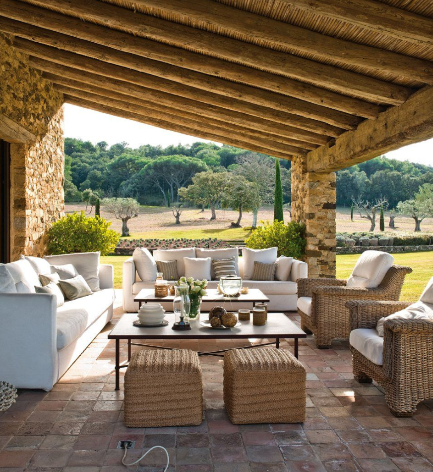 Terraza-Salón con sofas blanoc, mesas de cristal y sillones y pufs de paja, decoración elegante y rustica con flores y piedra.
